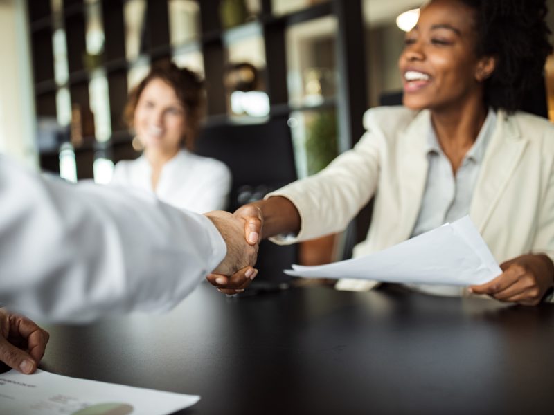 Executive woman smiling and shaking hands during a successful job interview, holding a resume.
