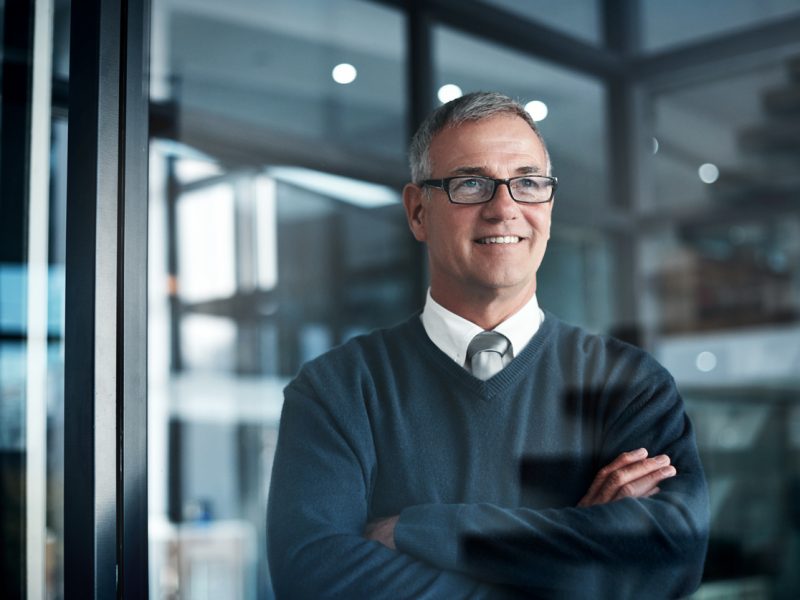 Confident senior executive standing in a modern office, arms crossed