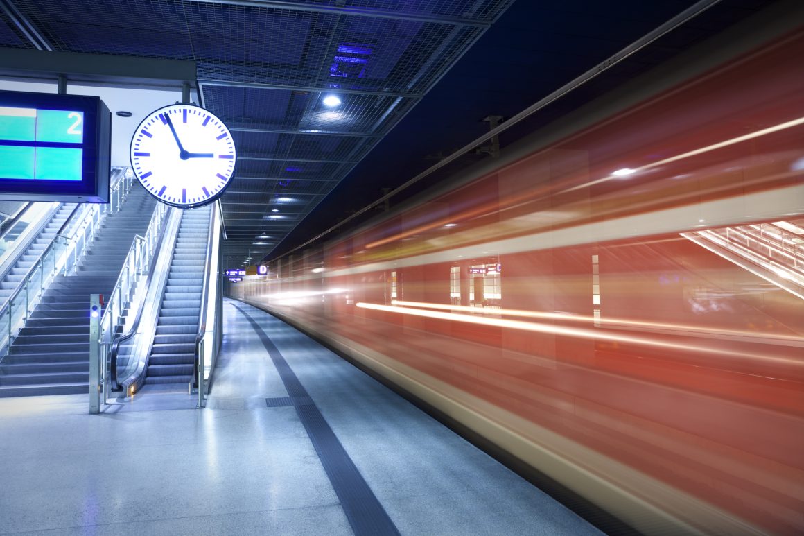 Blurry train speeding past a station clock, symbolizing the urgency of resume reviews in executive hiring.